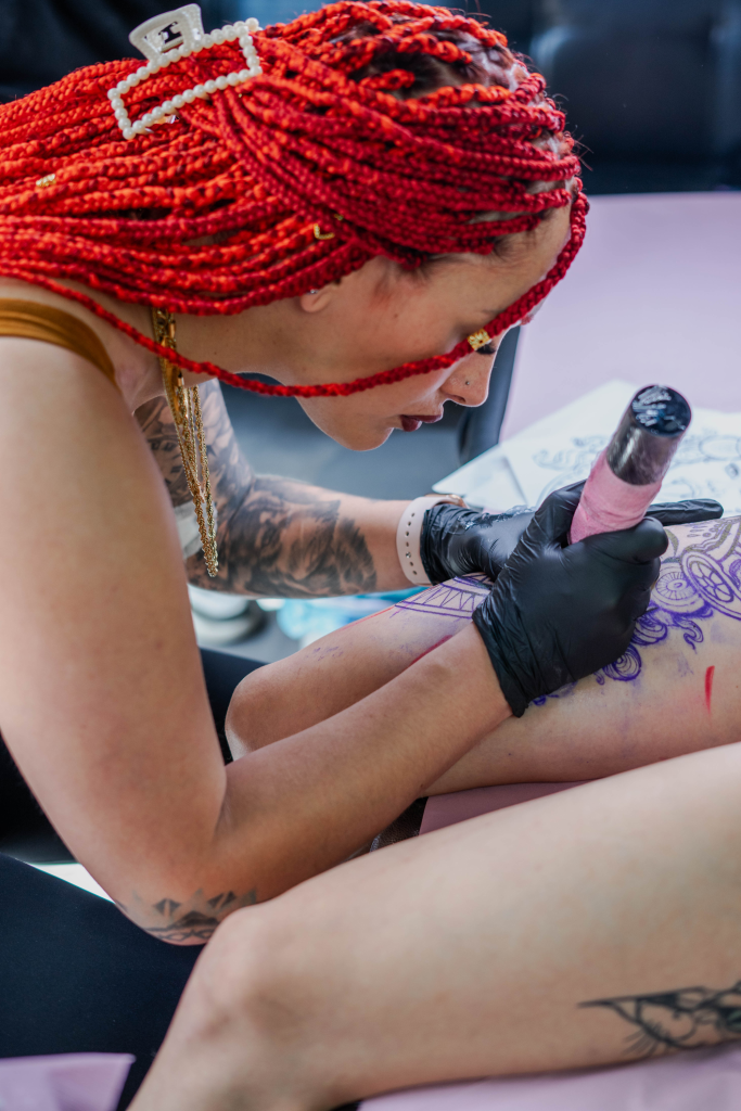 Sandy tatuando el antebrazo de una clienta, visto desde arriba, con la plantilla del diseño aún marcada en la piel