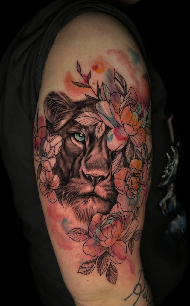Tatuaje a color de la cabeza de un león rodeada de flores rosas en el brazo